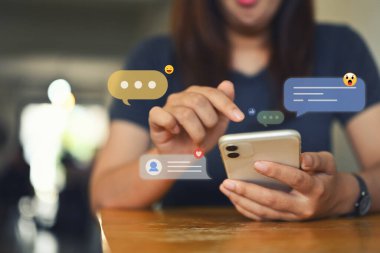 Mesaj, yorum ve benzeri mesaj simgeleriyle cep telefonu kullanan genç bir kadın. Sosyal medya ve teknoloji kavramı.