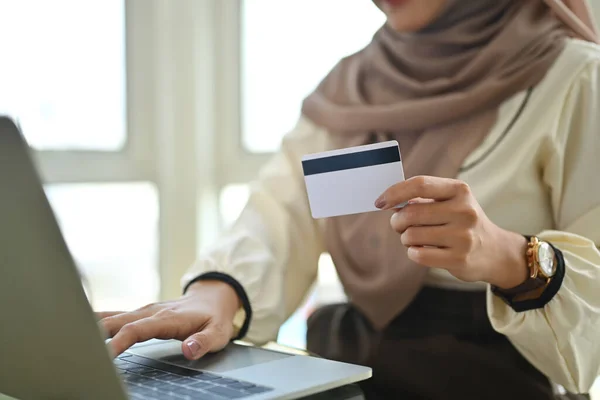 Muslim woman holding credit card using laptop doing online banking transaction or shopping in online store..
