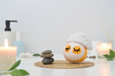 Yüz maskeli turuncu, beyaz arka planda zen taşları, mumlar ve yeşil yapraklar. Spa tedavisi ve kişisel bakım kavramı.