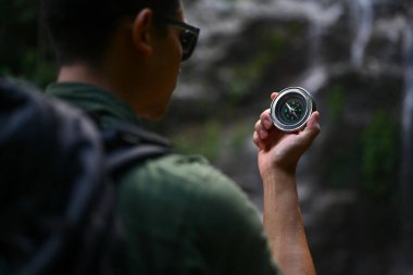 Ormanda yürüyüş yaparken pusula kullanarak sırt çantalı bir erkek gezginin arka görüntüsü..