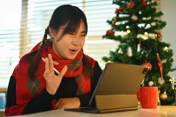 坐在装饰过的圣诞树旁 快乐的年轻女子通过数码平板电脑打来视频电话 — 图库照片