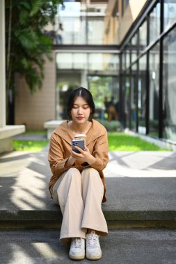 Güzel Asyalı bir kadının portresi iş merkezinin önünde oturuyor ve cep telefonu kullanıyor..