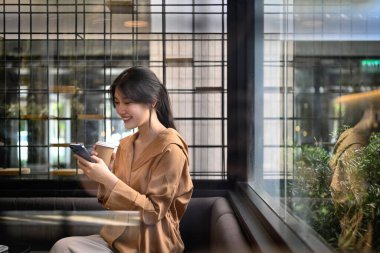 Çekici Asyalı kadın kahve içiyor ve modern kahve dükkanında cep telefonu kullanıyor. Kentsel yaşam tarzı konsepti.