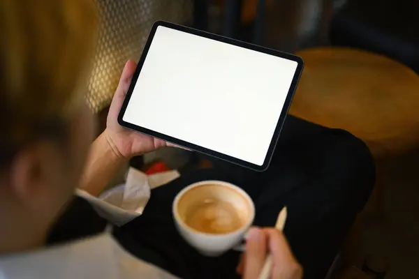 Cropped shot of young man drinking coffee and using digital tablet at modern coffee shop.