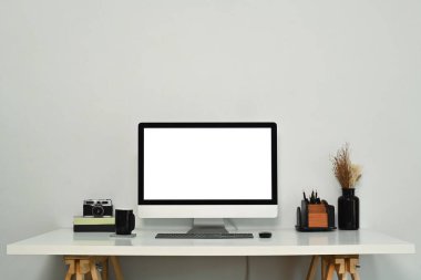 Boş ekran bilgisayar monitörü, kamera, kitap ve kahve fincanı beyaz masanın üzerinde olan yaratıcı iş yeri.