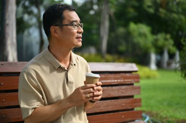 Elinde kahve bardakları olan orta yaşlı bir adam doğa parkının tadını çıkarıyor..