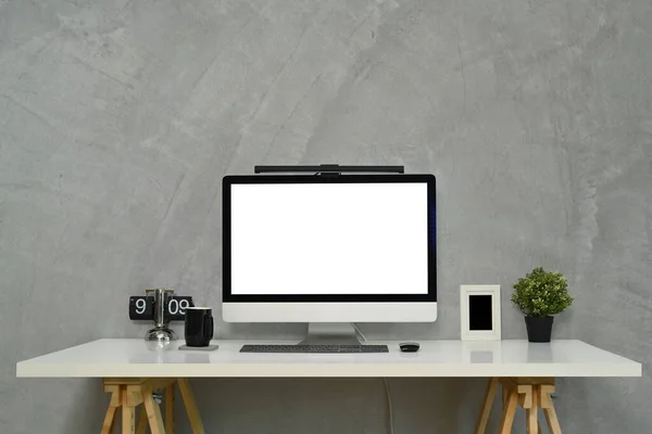 Stylish workplace with blank computer monitor, clock and houseplant on gray concrete background.
