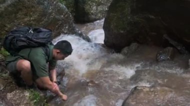 Erkek yolcu ellerini bir dağ deresinden gelen soğuk suyla yıkıyor..