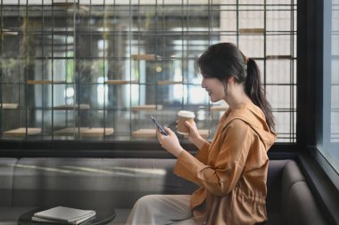 Modern ofis salonunda cep telefonu kullanarak kahve ısmarlayan güzel iş kadınının yan görüntüsü..