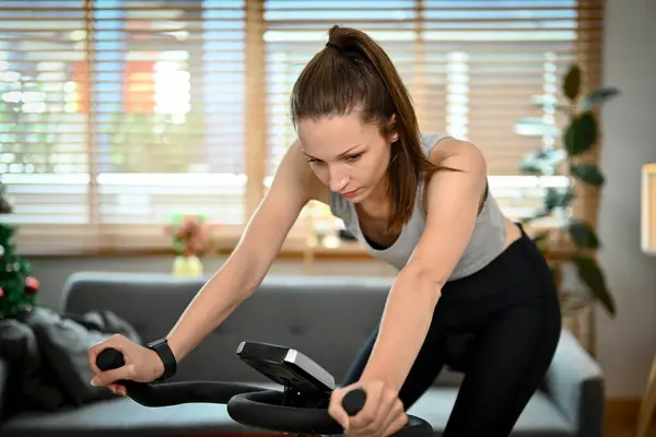 Portrait beautiful sportswoman cycling stationary bike exercise indoors for cardio workout.