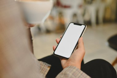 Kahve içen ve sosyal medyayı cep telefonundan kontrol eden genç bir iş kadını..