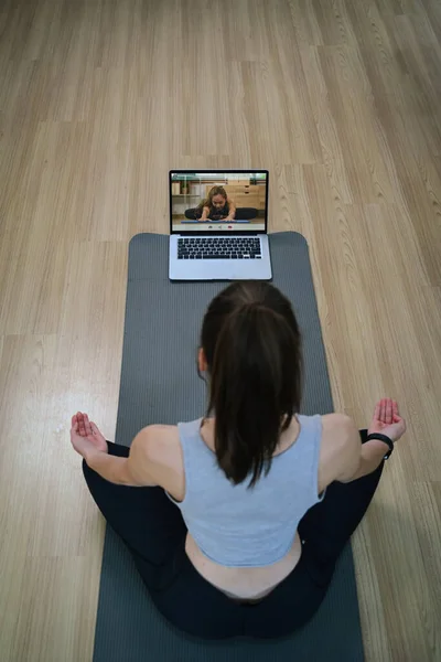 Above view of young woman doing yoga exercise and watching tutorial lesson on laptop at home.