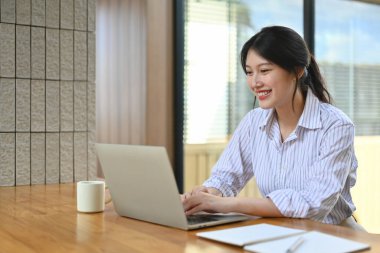 Gülümseyen genç bayan yönetici e-postaları kontrol ediyor ya da dizüstü bilgisayardan bilgi arıyor.