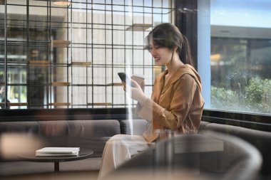 Modern ofis salonunda cep telefonu kullanarak kahve ısmarlayan güzel iş kadınının yan görüntüsü..