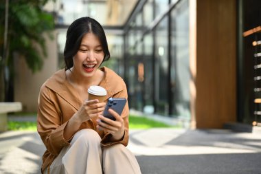 Ofis binasının yanında otururken cep telefonu kullanan neşeli Asyalı kadın..