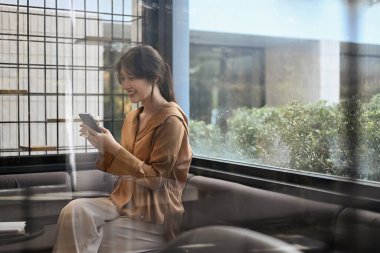 Modern ofis salonunda cep telefonu kullanan cam pencereli iş kadınına bakın..