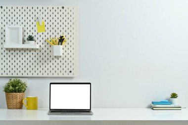 Boş ekranlı dizüstü bilgisayar, kahve fincanı, ev bitkisi ve beyaz masadaki kitaplar..