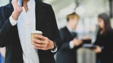 Ofis molasında elinde kağıt bardakla cep telefonuyla konuşan iş adamı..