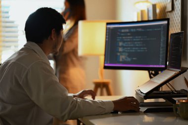Karanlık ofisteki masaüstü bilgisayarına odaklanmış yazılım geliştiricileri.