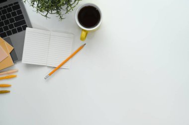 Dizüstü bilgisayarı, not defteri ve kahve fincanı olan beyaz ofis masası. Kopyalama alanı olan üst görünüm.