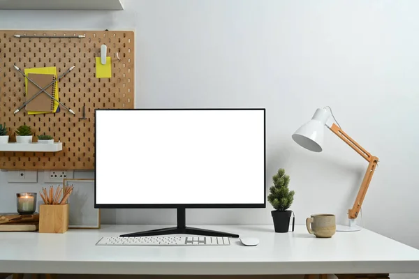 Creative workspace with blank computer desktop, lamp and stationery.