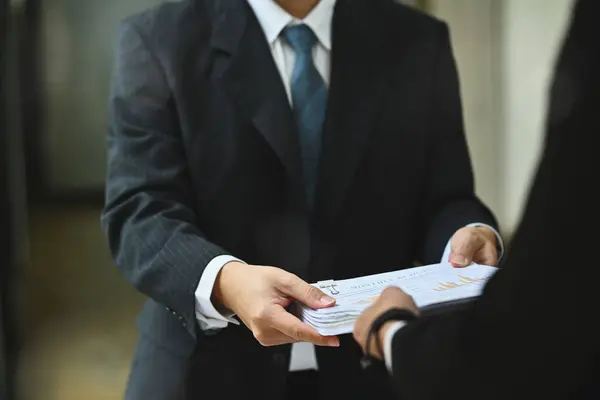 Financial inspector hands handing document to his colleague in office corridor.