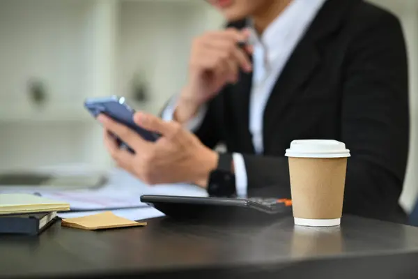 A take away coffee and calculator on office desk with blurred businessman using mobile phone on background.