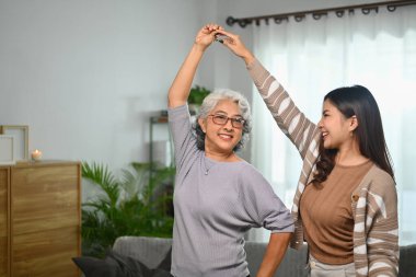 Mutlu gri saçlı orta yaşlı anne evde neşeli yetişkin kızıyla eğleniyor..
