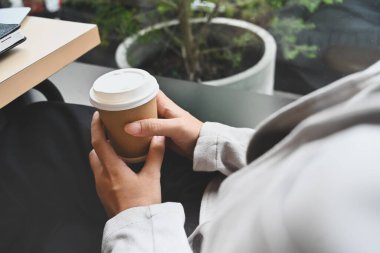 Kâğıt bardaklı iş kadını kafenin ya da restoranın penceresinin yanında dinleniyor..