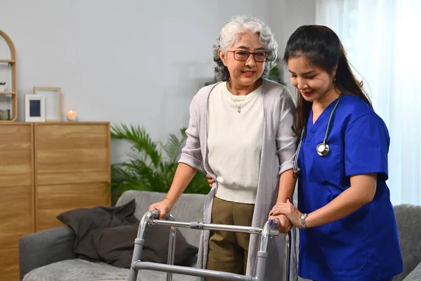 Female nurse helping senior woman to walking in her home with walker.