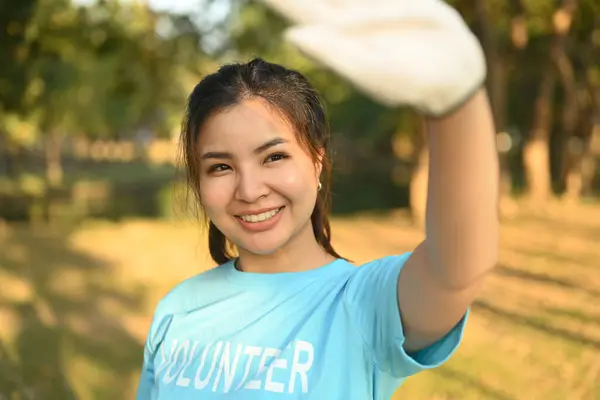 Positive Asian female volunteer cleaning up nature in sunny day. Charity and ecology concept.