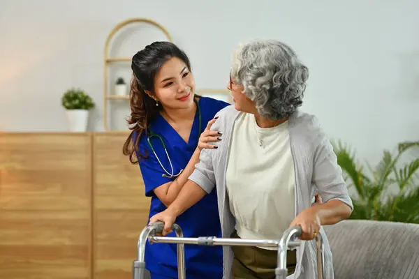 Female healthcare worker helping senior walking with walker in retirement home. Healthcare concept.