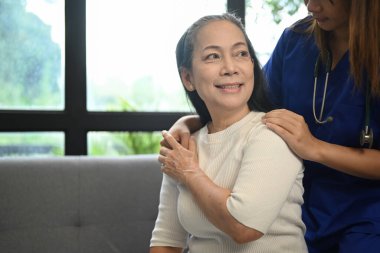 Orta yaşlı hastanın omzuna dokunan pratisyen hekim ev ziyareti sırasında psikolojik destek veriyor.