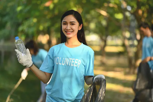 Beautiful female volunteer with garbage bag cleaning up the forest. Charity and ecology concept.