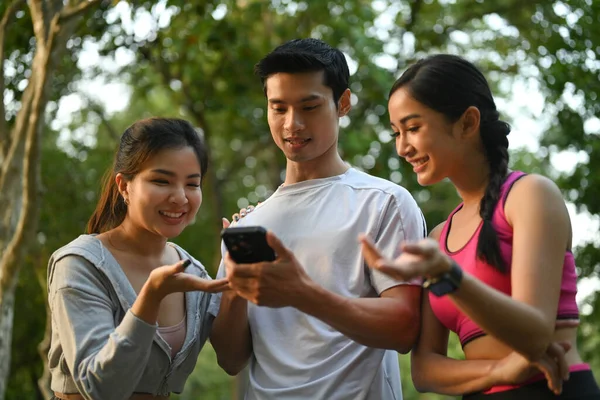 Happy athletic friends using mobile phone for tracking their fitness results at outdoor