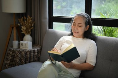 Hoş, orta yaşlı bir kadın evdeki kanepede dinleniyor ve günlüğünü yazıyor..