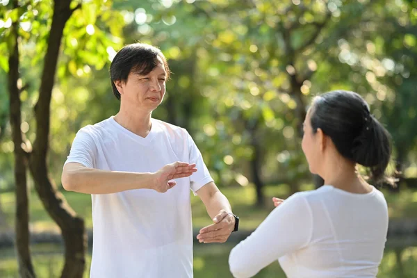 Happy senior people breathing fresh air while practicing Tai Chi Chuan in the park. Health care concept.