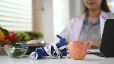 Dambıl ve elmayı beyaz masaya sarmış ölçü bandı. Diyet ve sağlıklı yeme konsepti