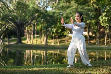 Gün doğumunda göl kenarında Qigong antrenmanı yapan gülümseyen yaşlı bir kadın.
