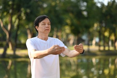 Chi Kung ya da Tai Chi alıştırması yapan kıdemli bir adam gün doğumunda göle karşı duruyor.