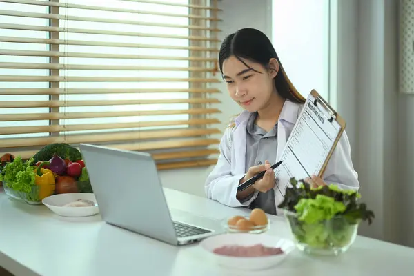 女营养师在笔记本电脑前展示剪贴板 向病人解释瘦身计划的细节 — 图库照片