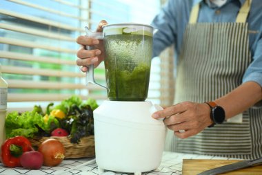 Orta yaşlı bir adam mutfakta blender ile sağlıklı meyve püresi yapıyor. Sağlıklı yaşam tarzı ve diyet konsepti