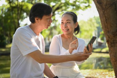 Mutlu son sınıf çifti güzel bir bahar gününde parkta otururken cep telefonu kullanırken eğleniyor.