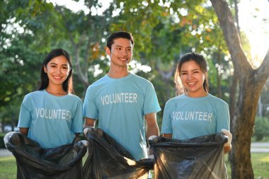 Güneşli bir günde çöp torbalarıyla doğayı temizleyen bir grup genç gönüllü. Hayırseverlik ve ekoloji kavramı