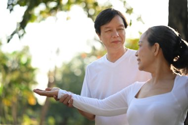 Beyaz elbiseli aktif orta yaşlı çift parkta Tai Chi ile çalışıyor. Sağlık ve refah kavramı