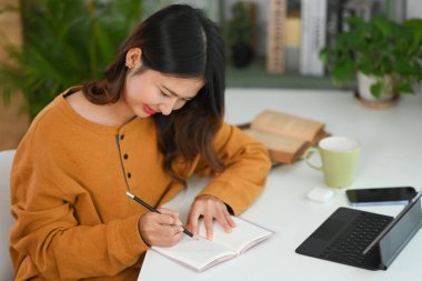 Güzel genç Asyalı kadın çalışma masasında günlük randevu planlarken önemli notlar alıyor.