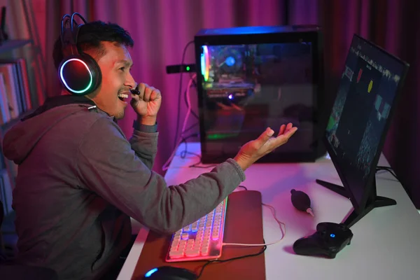 Cheerful gamer streamer playing online video game and chatting with his teammates through headphones