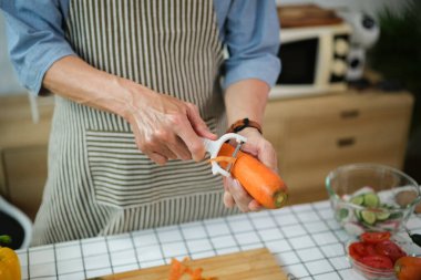 Önlük giymiş, havuç soyan, mutfakta sağlıklı salata hazırlayan kıdemli bir adam..
