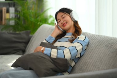 Kaygısız genç kadın evde kanepede dinlenirken kapalı gözlerle müzikten zevk alıyor.