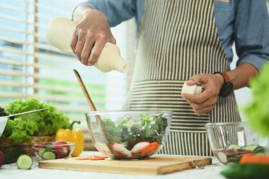 Kıdemli adam taze sebze salatasıyla kase içine sos dolduruyor. Sağlıklı beslenme ve aşçılık kavramı.